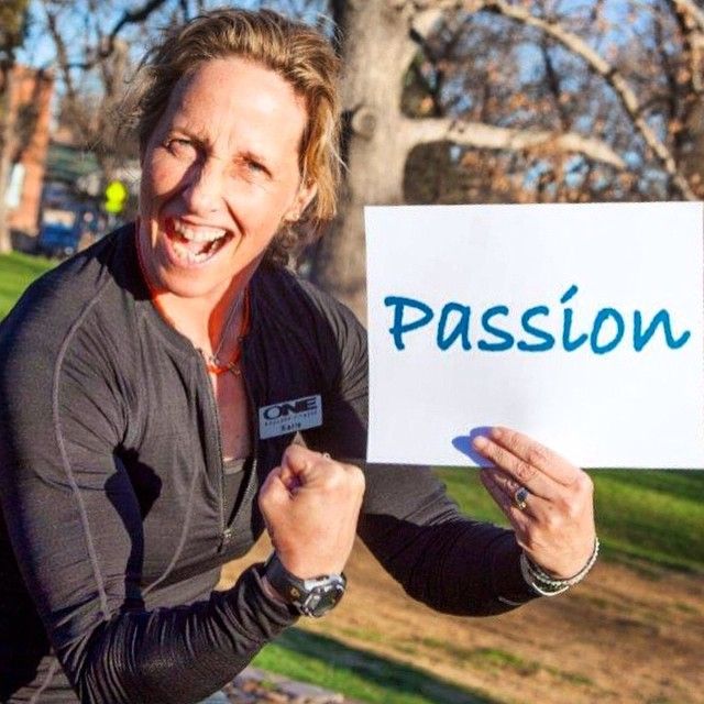 Karie, owner of ONE Boulder Fitness, laughing while holding a sign that reads “Passion”