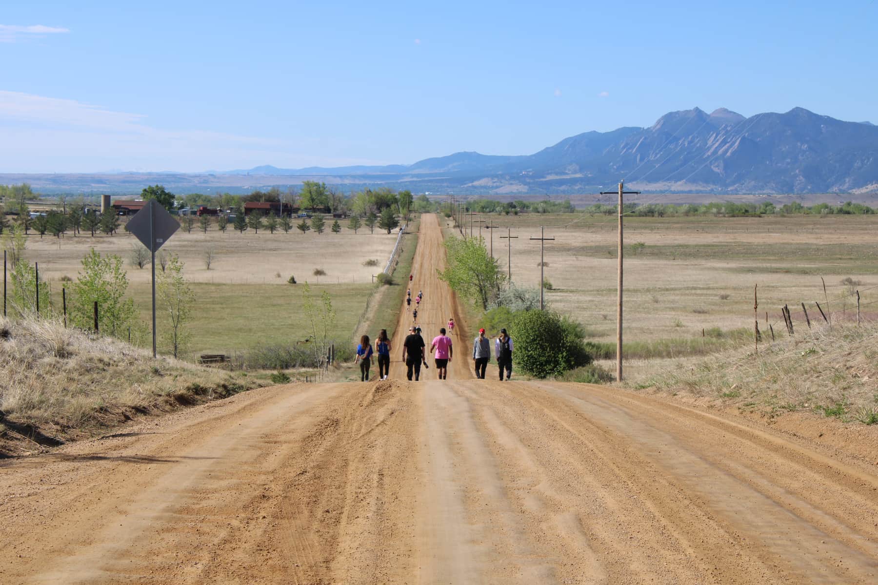 Group of walkers heading down a long dirt road with the Flatirons in the distance, Boulder, Colorado