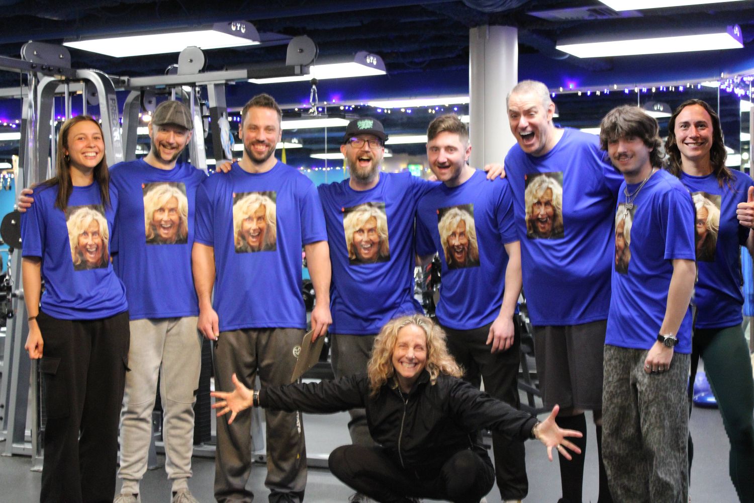 The whole trainer team on the gym floor in shirts printed with the owner’s face