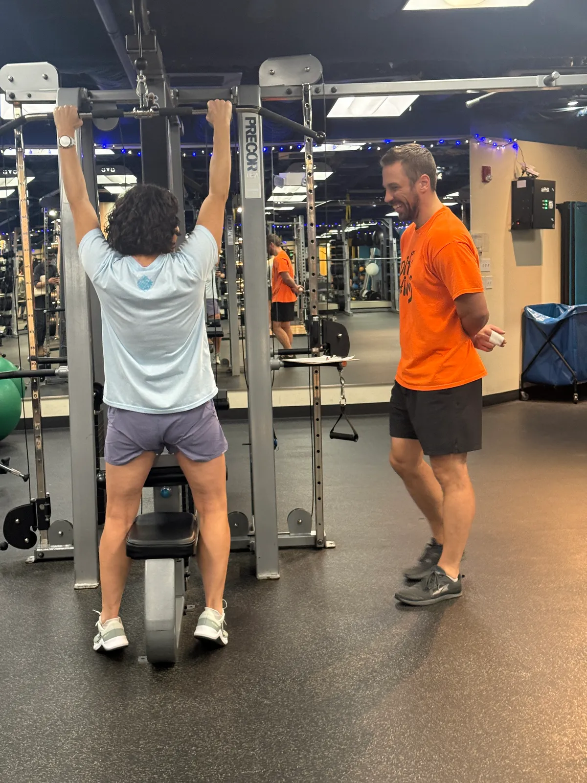 A ONE Boulder Fitness trainer smiling as he coaches a member through a lat pulldown